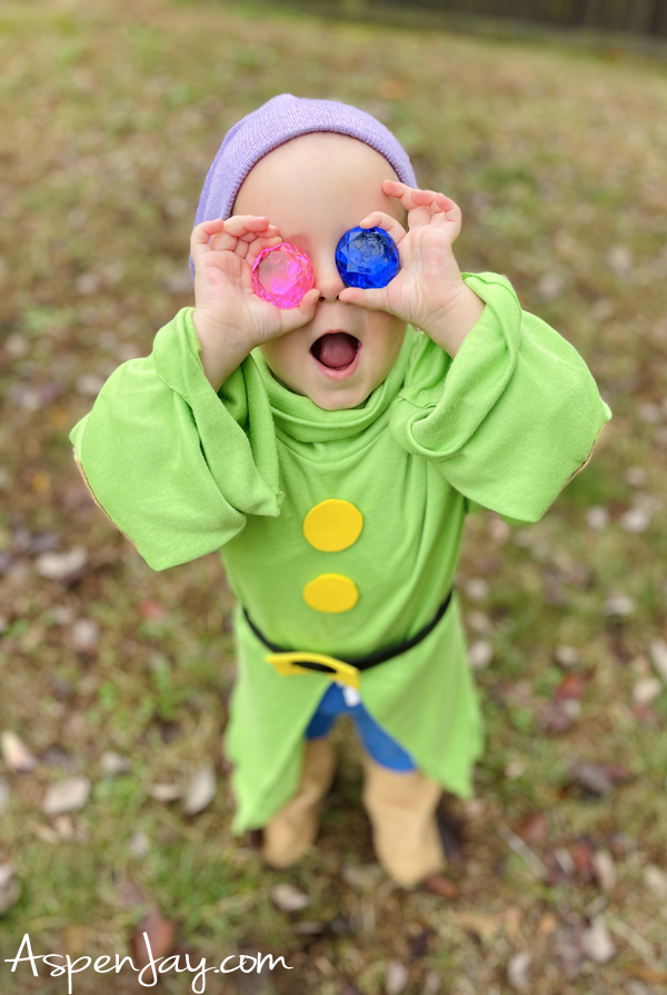 Child dressed in a DIY Dopey costume from Snow White and the Seven Dwarfs with green oversized turtleneck, lavender beanie, and playful pose