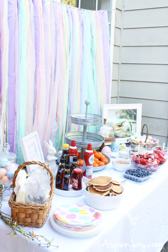 Easter party table setup with pancakes, fruit, decorations, and pastel backdrop