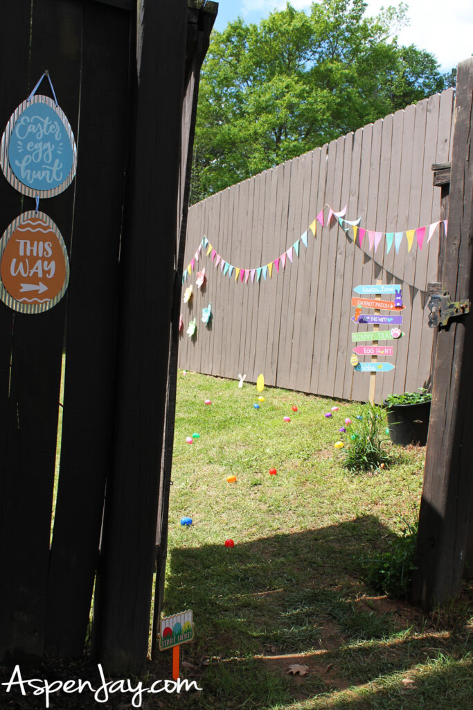 backyard Easter egg hunt entrance with decorations, signs, and eggs scattered on grass