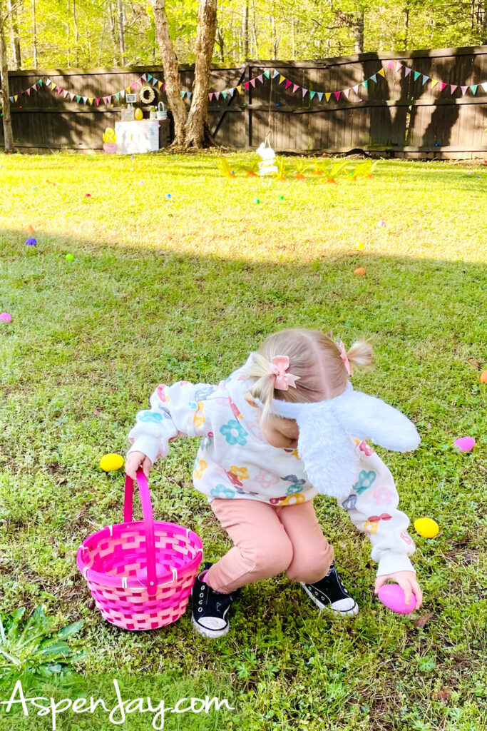 toddler collecting Easter eggs in backyard with pink basket during egg hunt