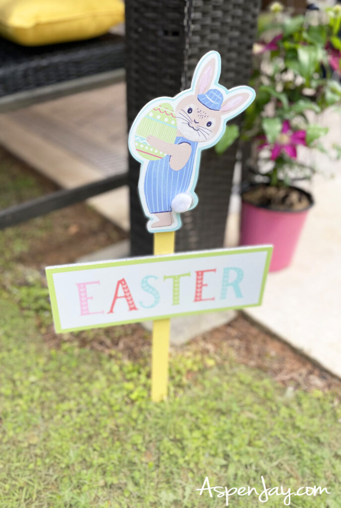 Easter yard sign with bunny holding egg and colorful spring decorations in grass